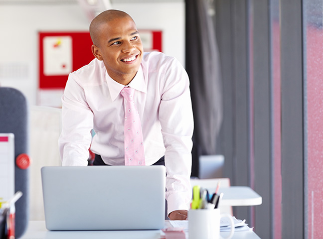 Employee Smiling And Standing By His Laptop After Choosing Health Insurance Plan