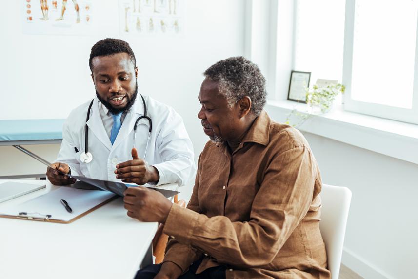 A man sits at a table alongside his doctor while they review health information together.