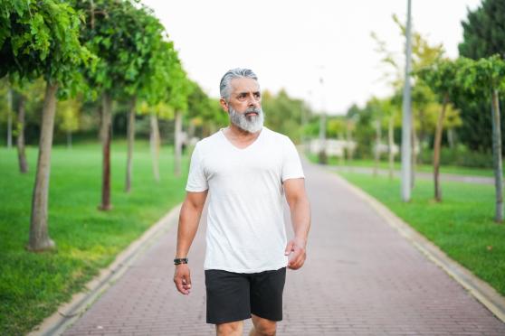 A man walks down an empty sidewalk wearing a white T-shirt and black shorts.