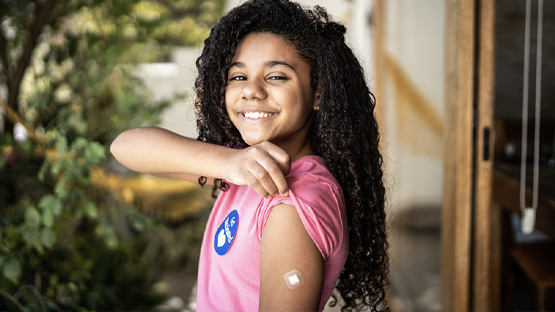 A smiling young girl shows her arm, having been vaccinated